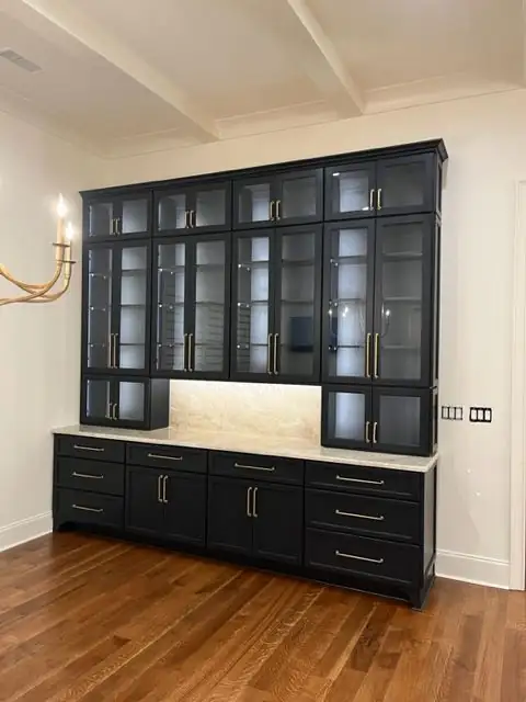 Black glass-front built-in cabinets with brass pulls, lit shelves and a stone countertop